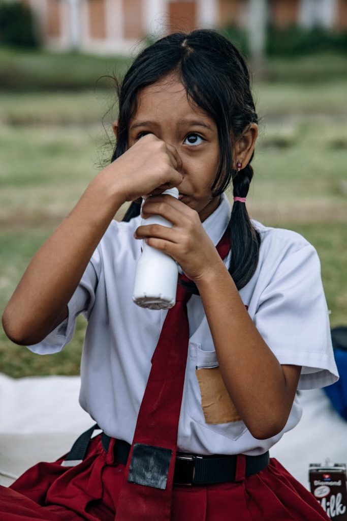 pexels-photo-12719242 Young girl in school uniform drinking milk outdoors, capturing childhood innocence.
