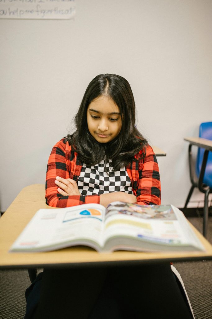 pexels-photo-6936177-6936177 A focused young girl reading a book at her desk in a classroom setting.